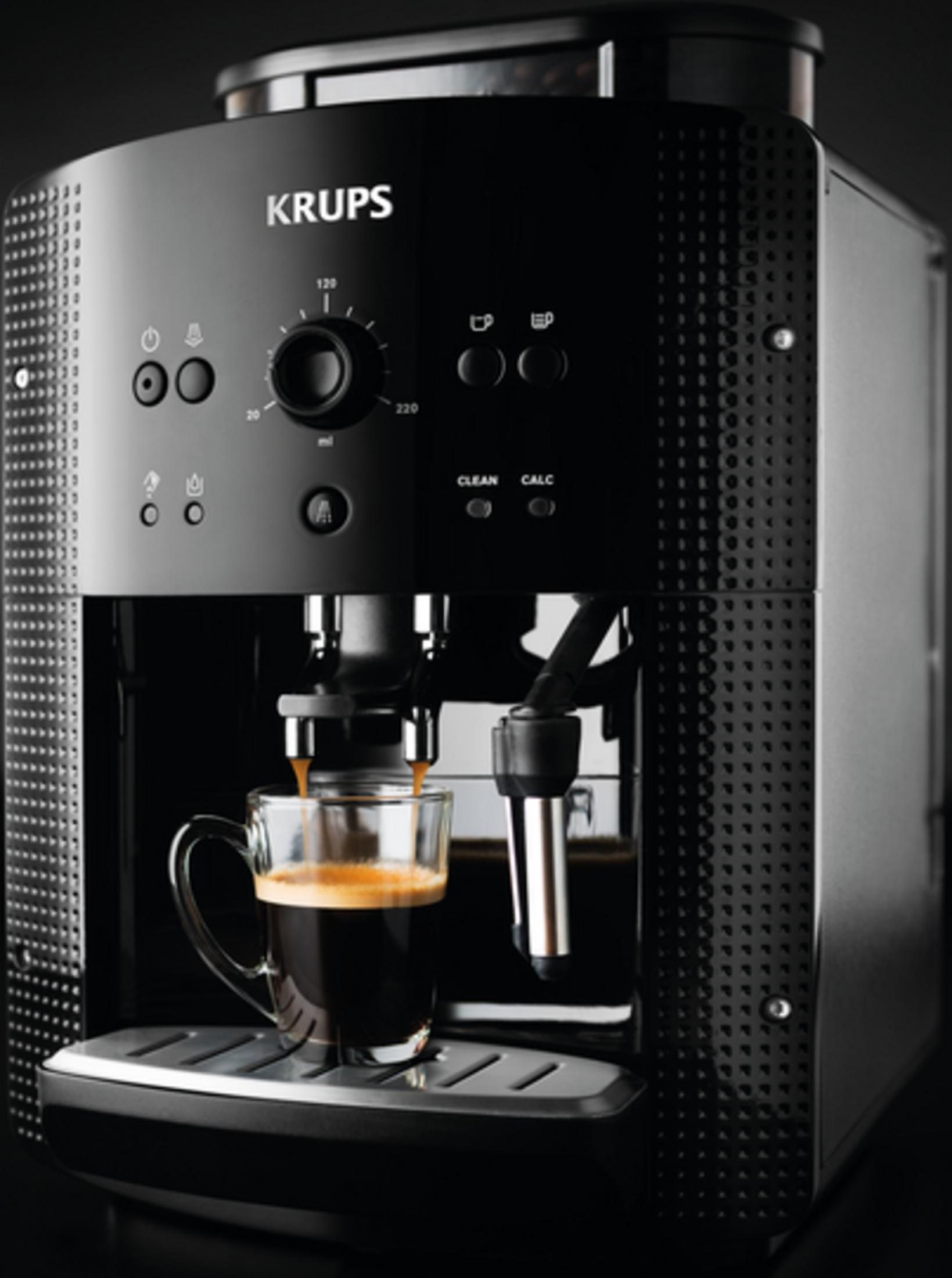 Schwarze Krups Kaffeemaschine brüht Espresso in eine Glastasse auf einem Edelstahlgitter.