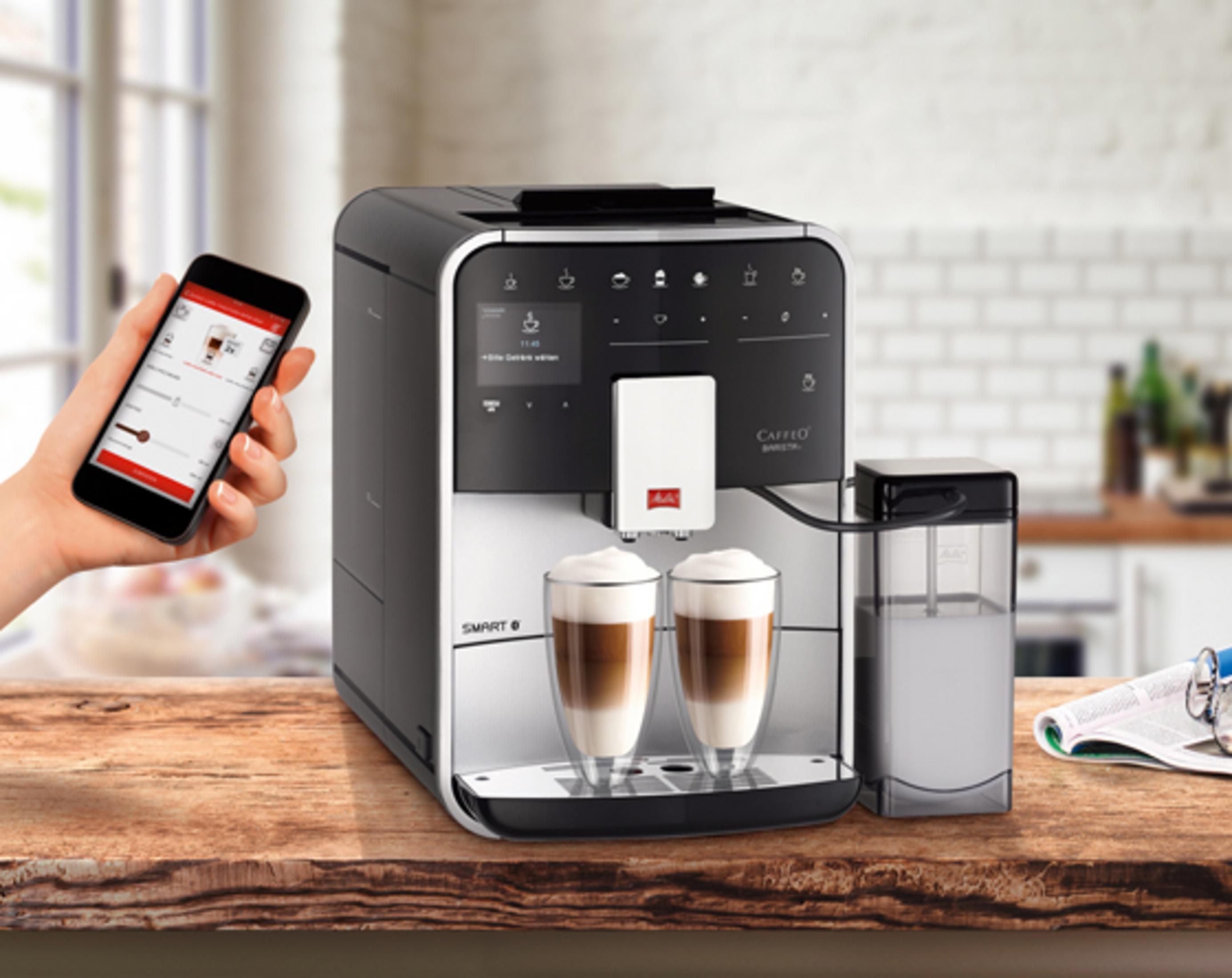 Modern coffee machine on a wooden table with two latte macchiato glasses and smartphone control.