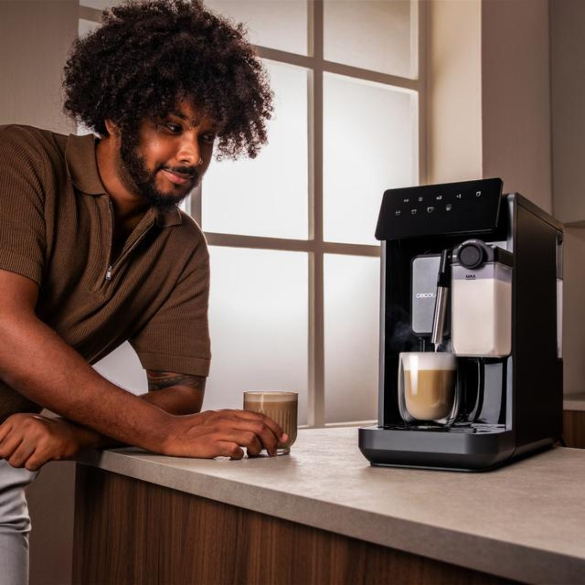 Un uomo con i capelli ricci guarda una moderna macchina da caffè nera che eroga un caffellatte.