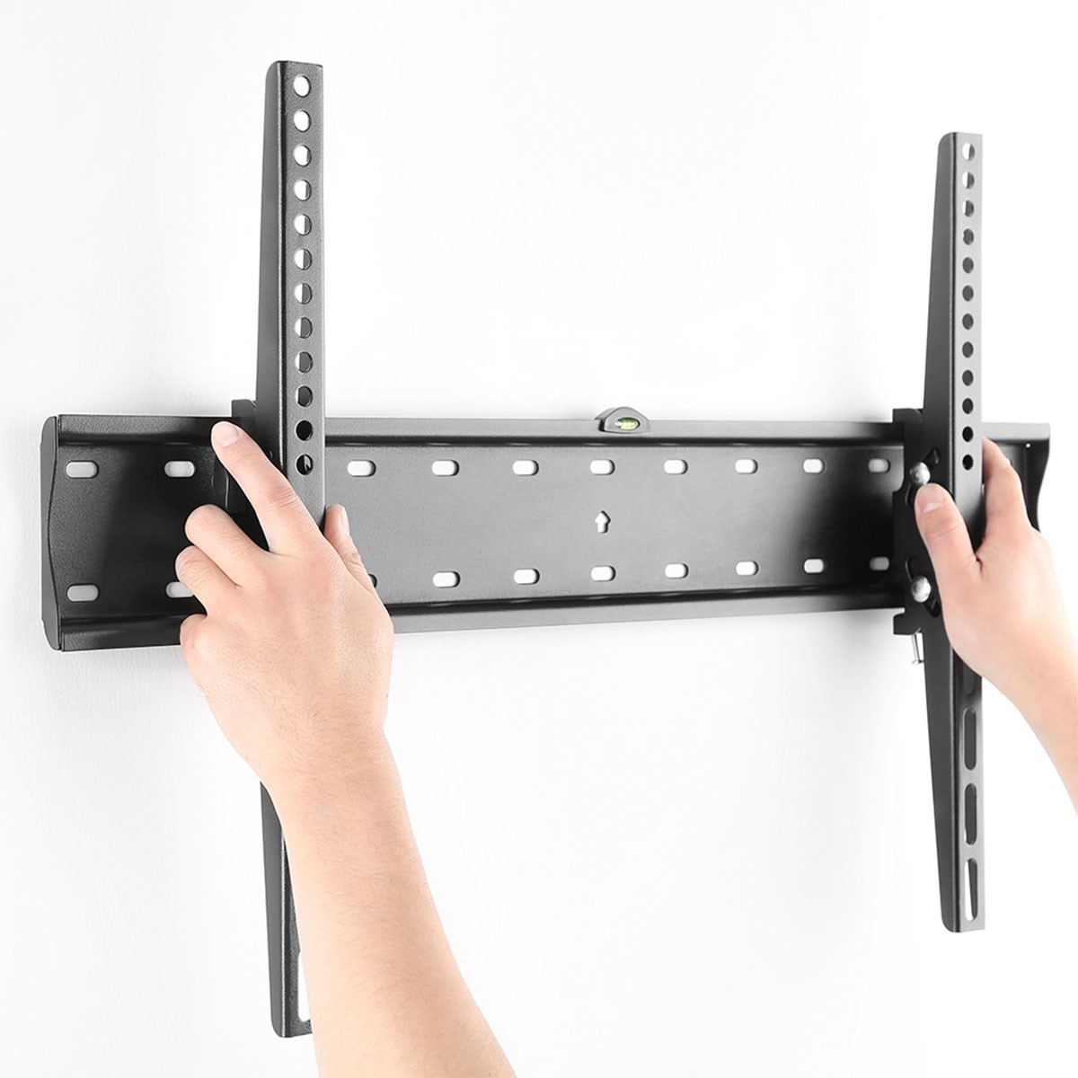 Manos sosteniendo un soporte de pared negro para TV contra una pared blanca.