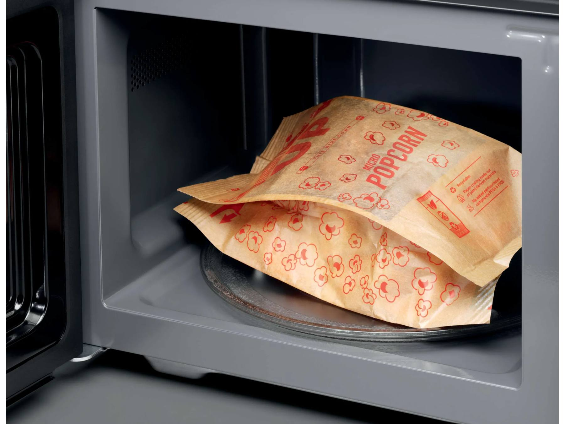Eine braune Papiertüte mit Mikrowellen-Popcorn liegt auf einem Glasteller in einer sauberen grauen Mikrowelle.