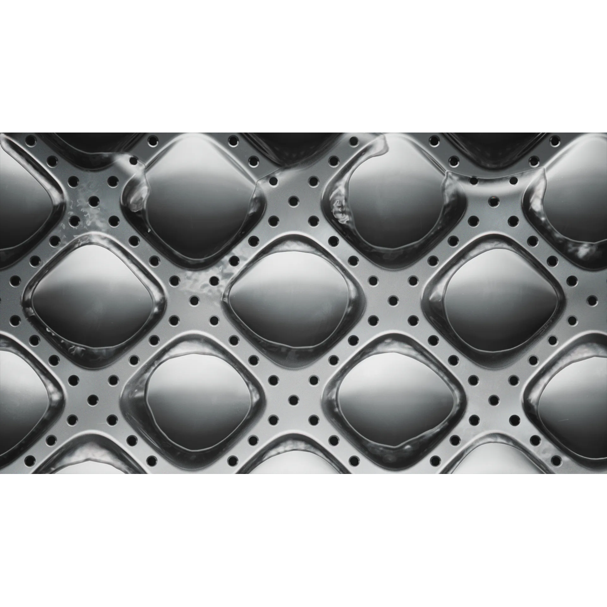 Primer plano del interior del tambor de una lavadora plateada con formas de diamantes y agujeros.
