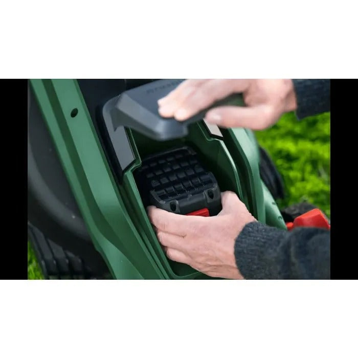 Eine Person setzt eine schwarze Batterie in ein grünes Rasenmäherfach ein.