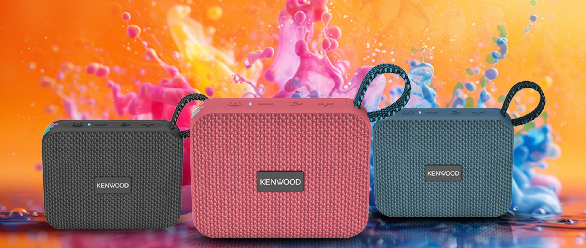 Three Kenwood portable speakers in black, pink, and blue against a vibrant orange and pink abstract background.