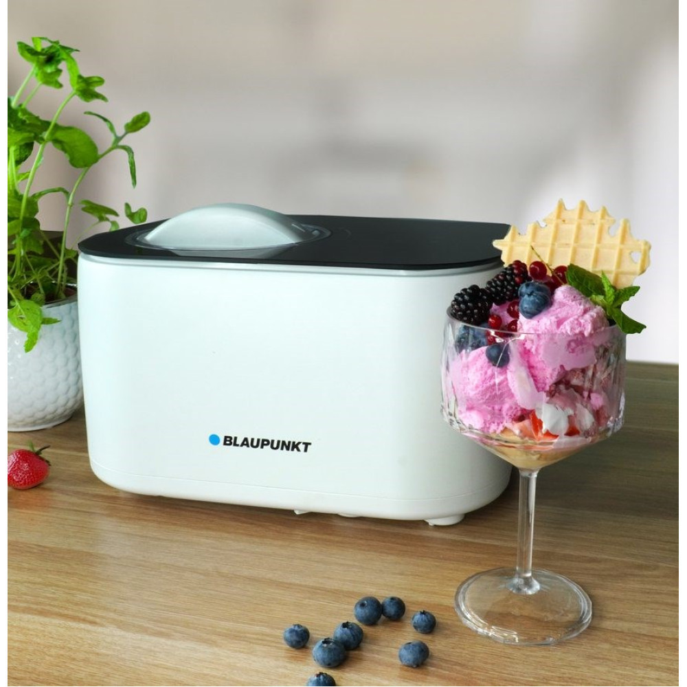 Eine weiße Eismaschine von Blaupunkt steht auf Holz, daneben ein Glas mit Beeren-Eis und frischen Blaubeeren.