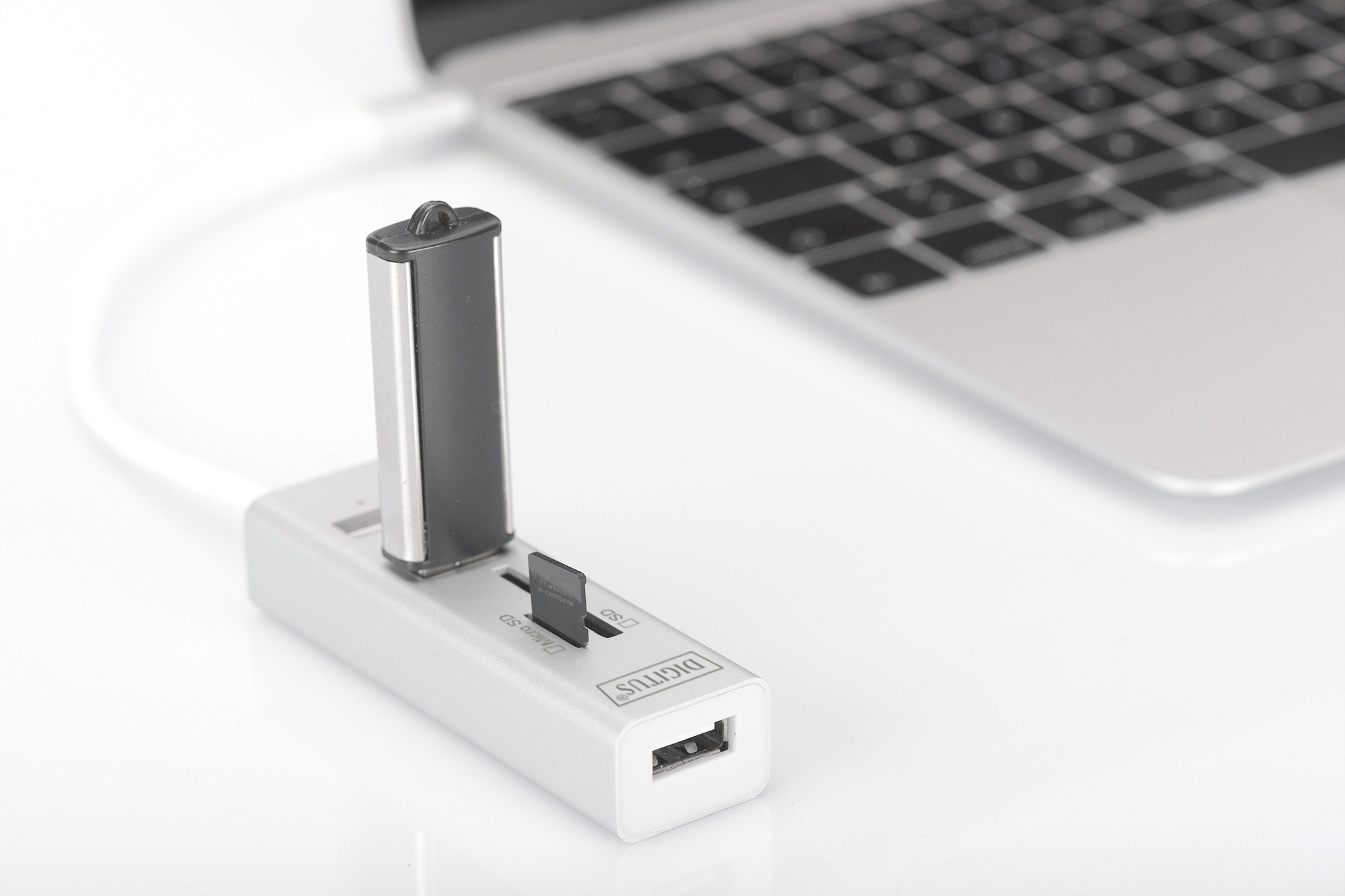 Ein silberner USB-Hub mit einem angeschlossenen USB-Stick und einer SD-Karte liegt vor einem Laptop.