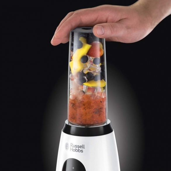 Siyah arka planda meyvelerle dolu beyaz bir Russell Hobbs blender'a basan el.