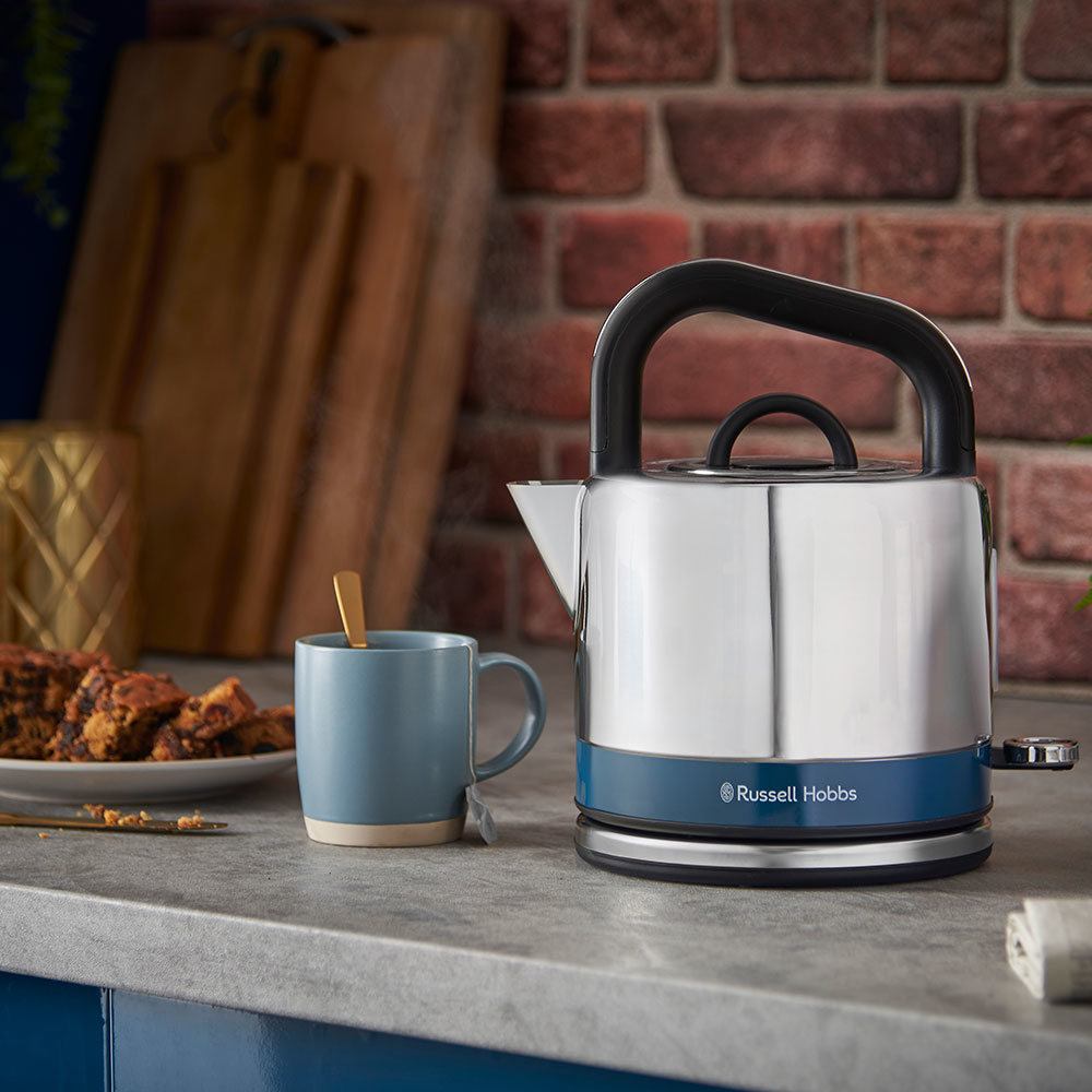 Tezgahta bir çay kupası ve kek ile mavi ve gümüş rengi bir Russell Hobbs su ısıtıcısı.