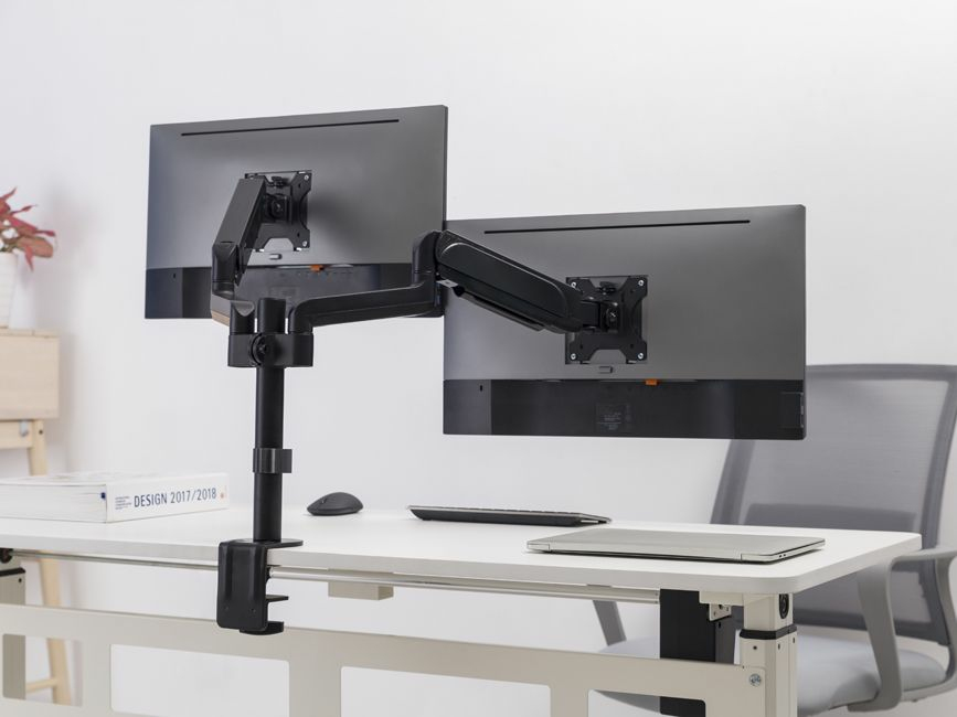 A black dual monitor arm is clamped to a white desk, holding two monitors.
