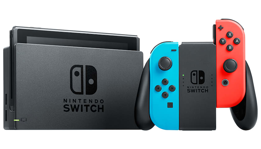 Una console Nintendo Switch nera nella sua base accanto a controller Joy-Con blu e rossi.