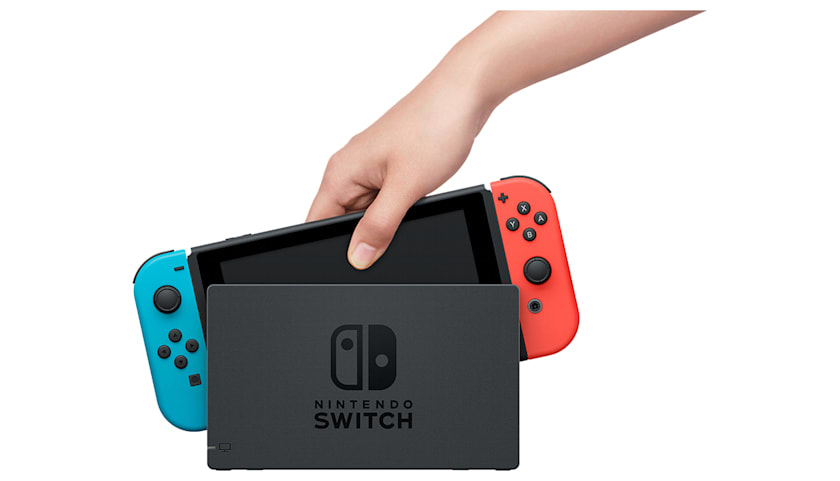 Una mano inserisce una console Nintendo Switch con controller Joy-Con blu e rosso nella dock nera.