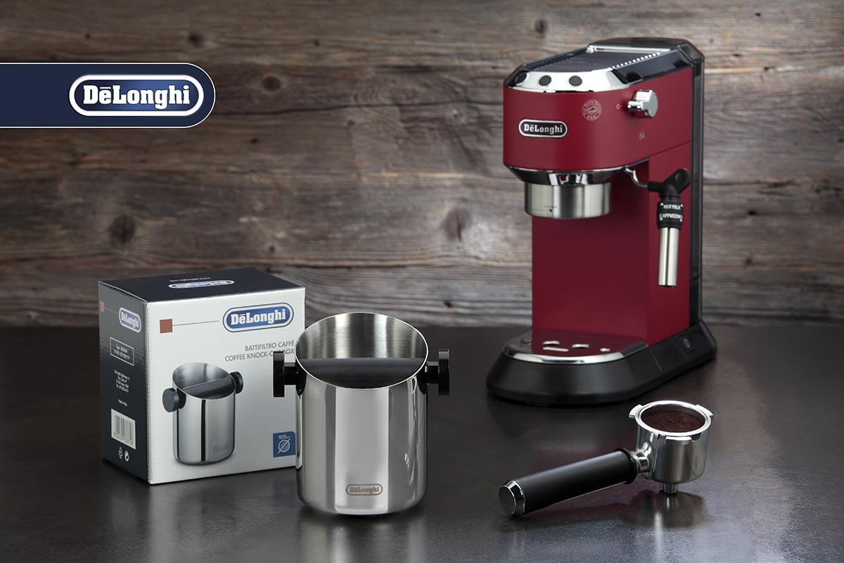 Machine à expresso DeLonghi rouge avec boîte à marc et porte-filtre sur une surface sombre devant un mur en bois.