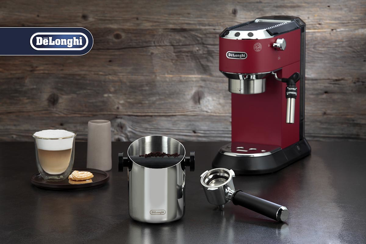 Machine à espresso rouge DeLonghi avec accessoires, cappuccino et café moulu sur plan de travail.