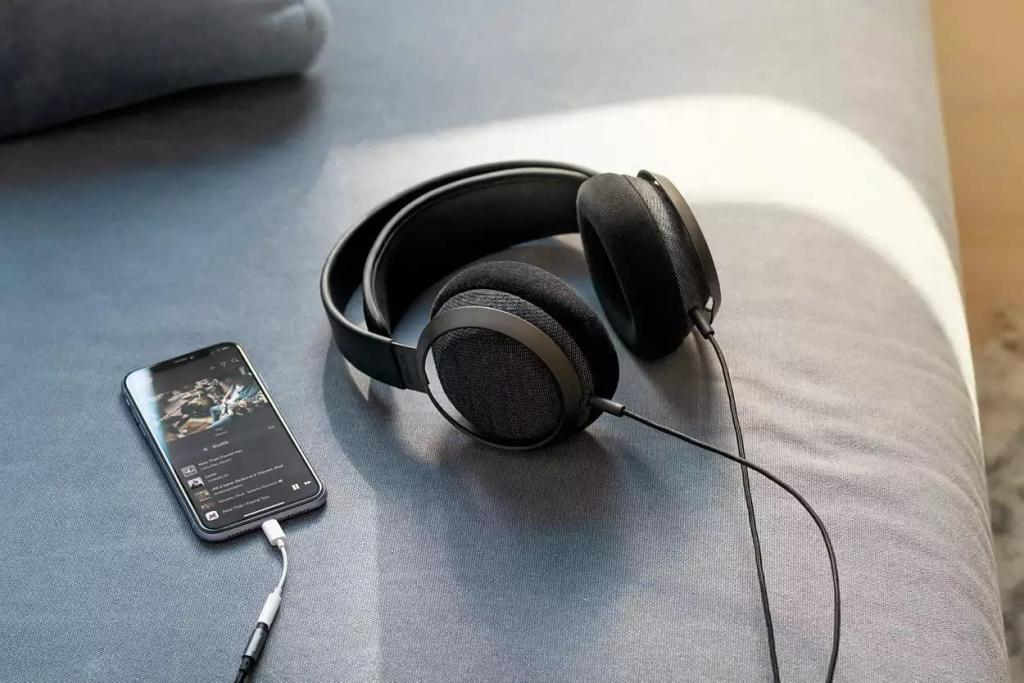 Schwarze On-Ear-Kopfhörer und ein Smartphone mit Musik-App liegen auf einem grauen Sofa.