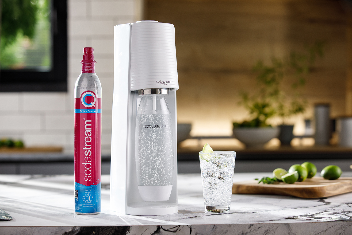 Weißer SodaStream, Gaskartusche und ein Glas Sprudelwasser mit Limette auf einer Küchentheke.
