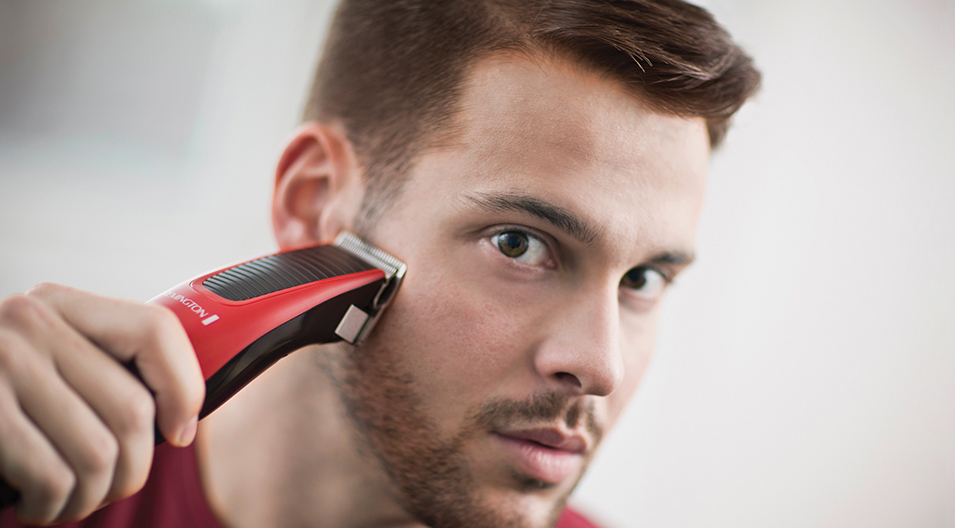 Ein Mann stutzt seinen Bart mit einem rot-schwarzen Trimmer.