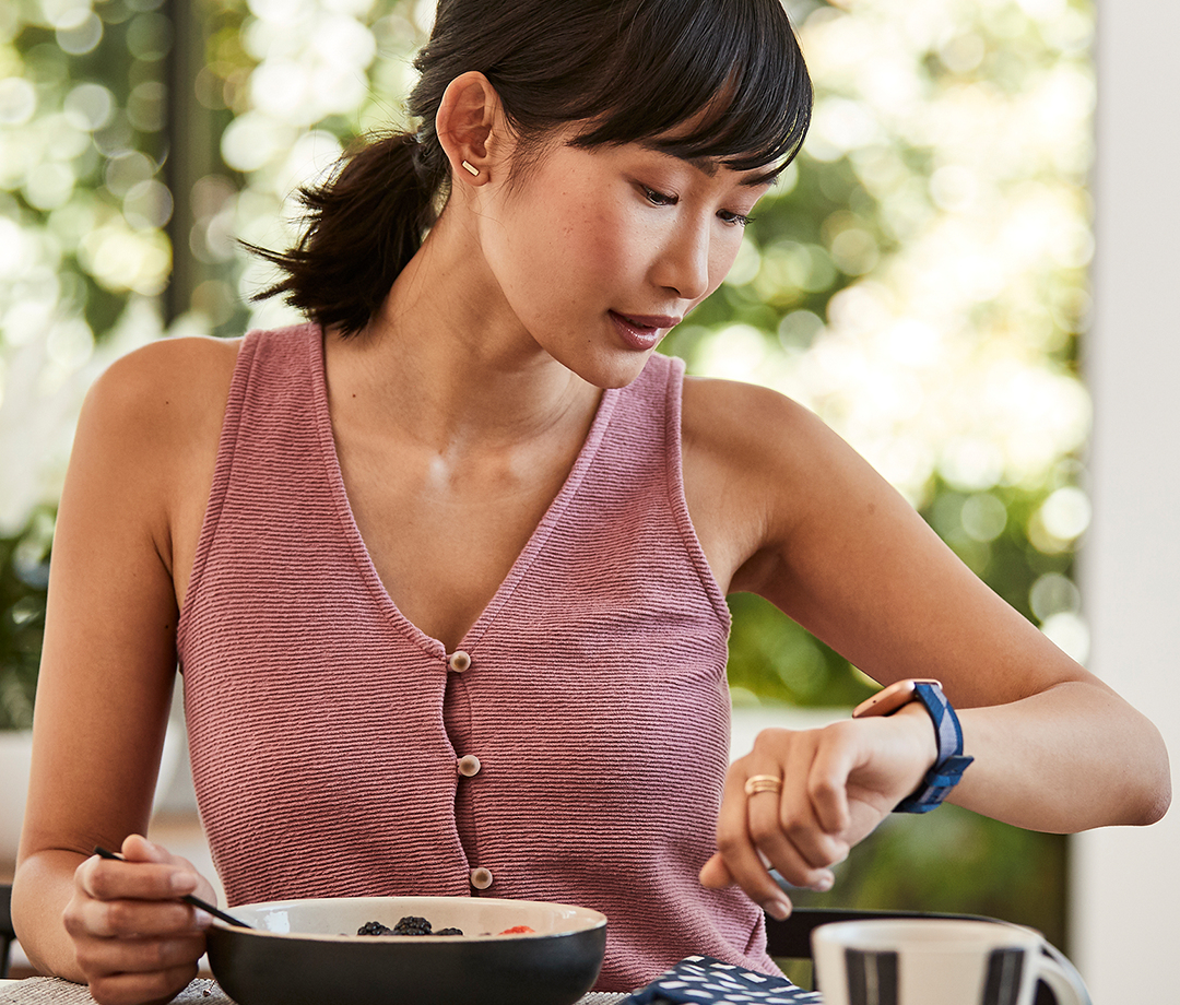 Eine Frau in einem pinken Top blickt auf ihre Smartwatch, während sie eine Schüssel mit Beeren isst.