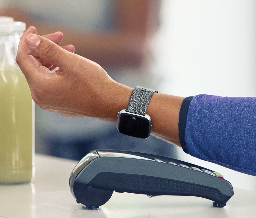 Person bezahlt kontaktlos mit einer Smartwatch an einem Kartenlesegerät.