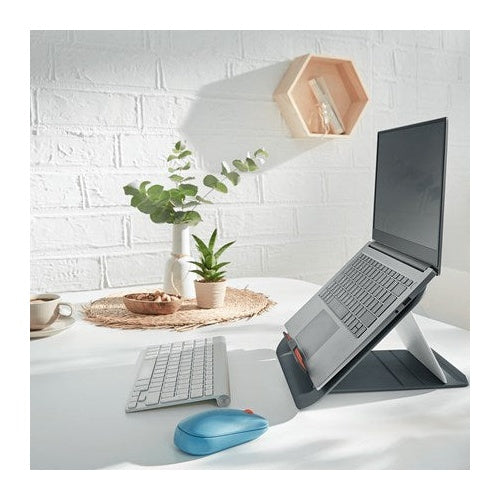 A laptop on a stand, a keyboard and a blue mouse on a desk in front of a white brick wall.