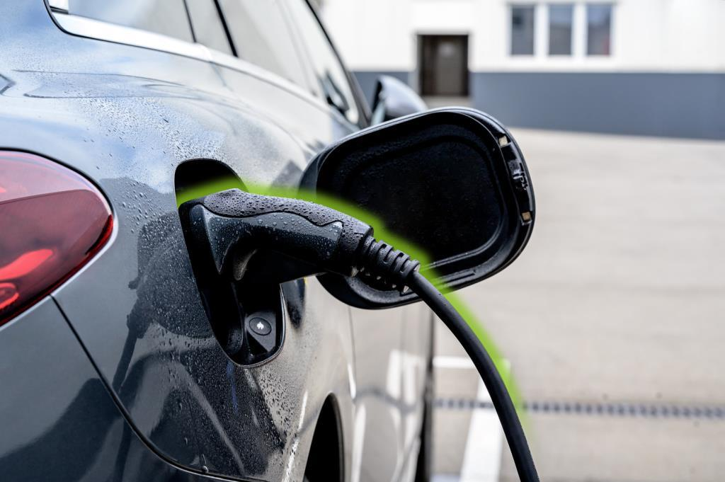 Gri renkli bir elektrikli araç şarj için takılı, gövdesinde su damlacıkları var.