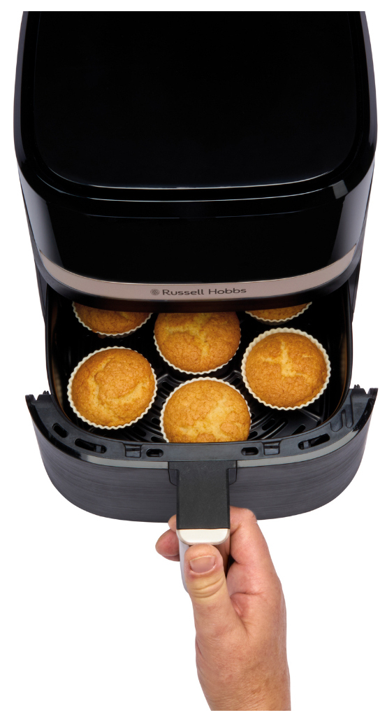 Una mano apre una friggitrice ad aria nera piena di muffin appena sfornati.