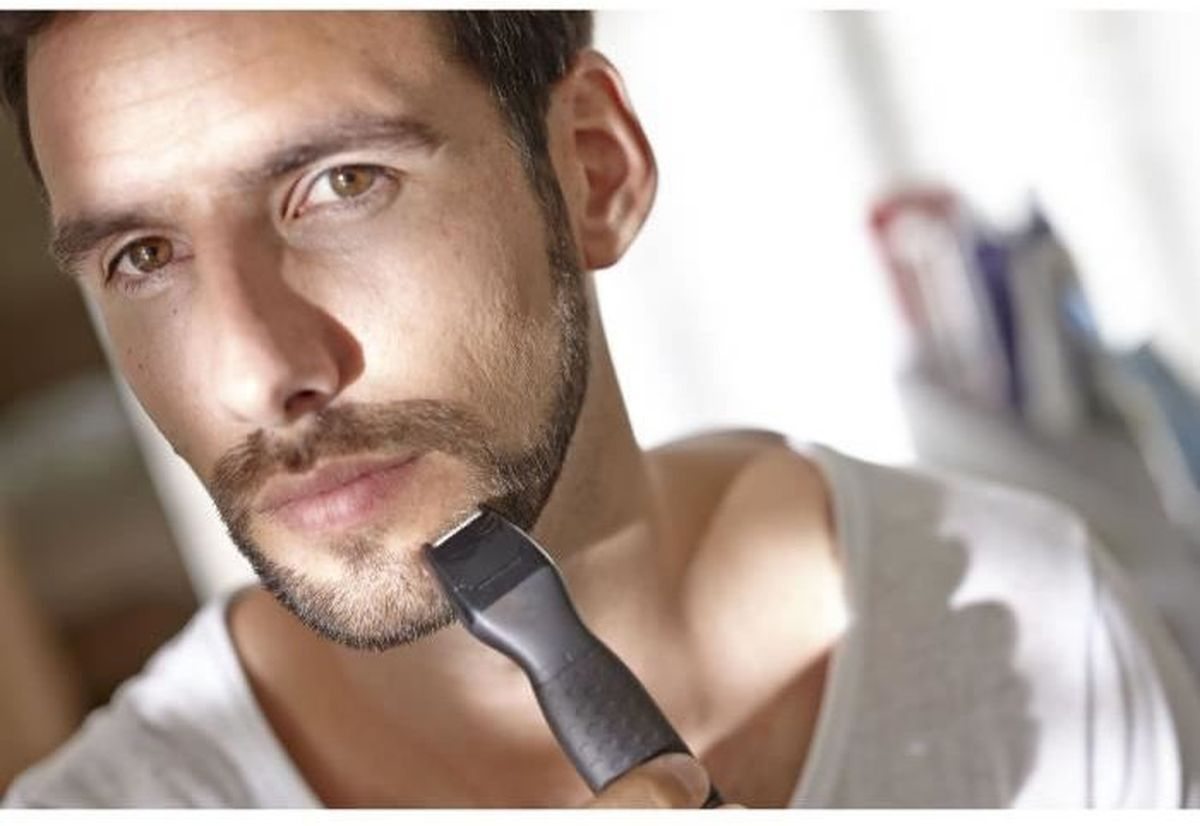Un hombre recortándose la barba con una recortadora negra.