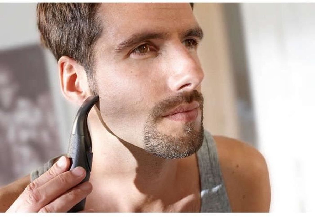 Un hombre recortándose la barba con una recortadora eléctrica pequeña.
