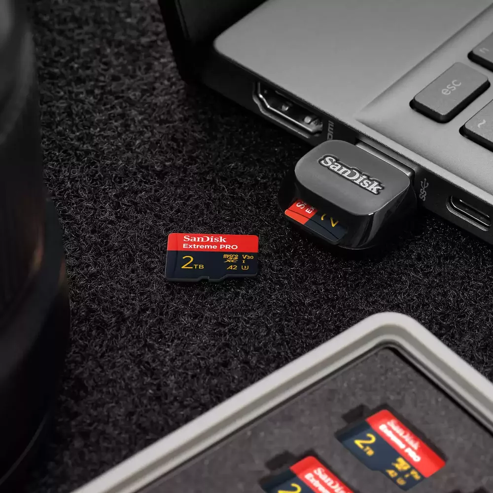 Una scheda micro SD SanDisk Extreme PRO da 2TB e un lettore USB accanto a un computer portatile.