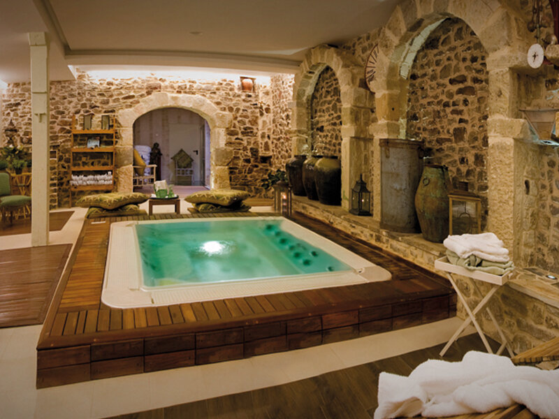Piscina de hidromasaje interior en una habitación de piedra rústica con detalles de madera y arcos.