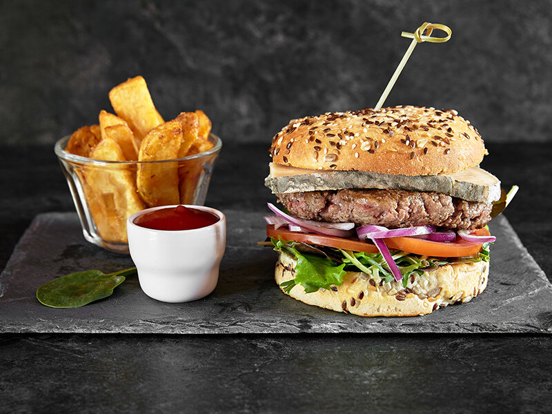 Una hamburguesa gourmet con patatas fritas y kétchup en una placa de piedra oscura.