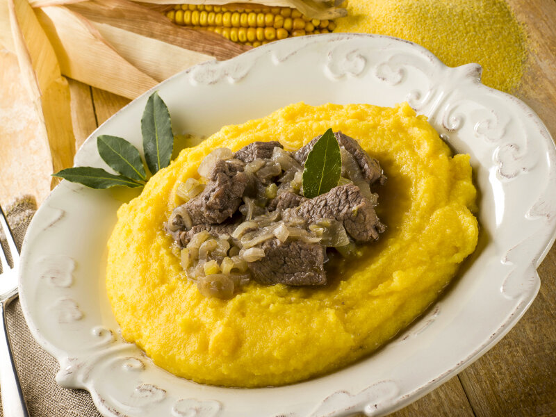 Polenta con carne de res estofada y cebolla en un bol blanco.