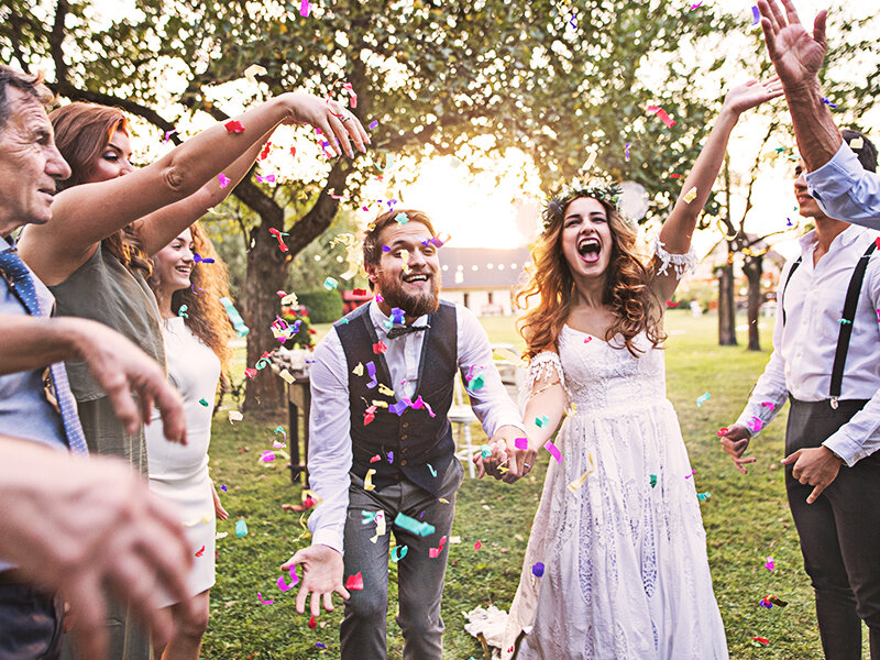 Los novios celebran con invitados al aire libre mientras confeti colorido vuela.