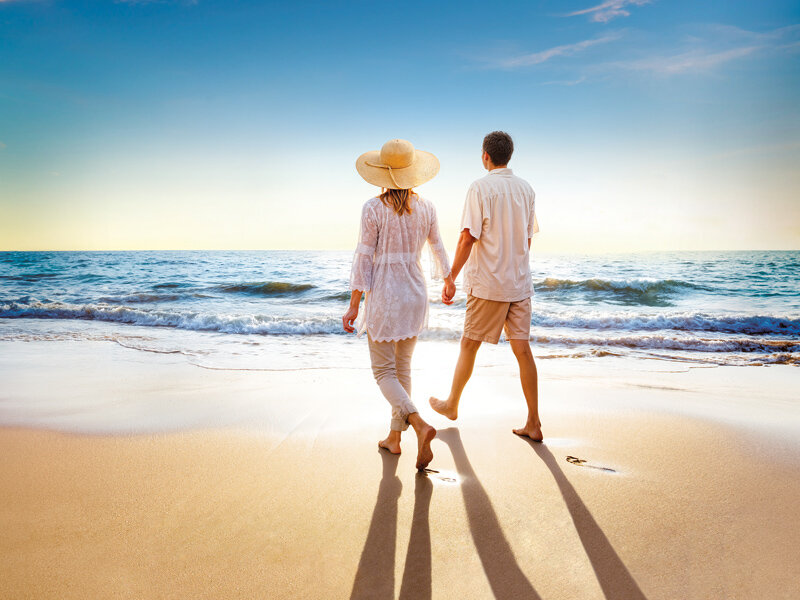 Una pareja camina de la mano por una playa de arena al atardecer.