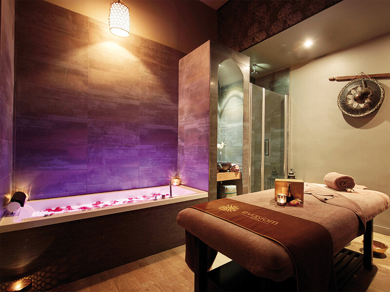 Lujosa sala de spa con una bañera iluminada con pétalos de flores y una camilla de masajes.