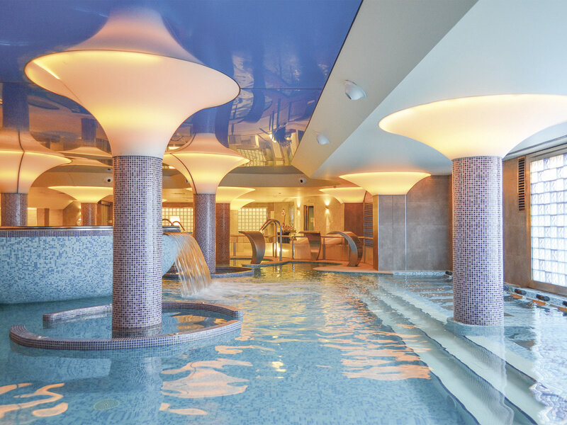 Piscinas de bienestar modernas con pilares de setas iluminados y azulejos azules.