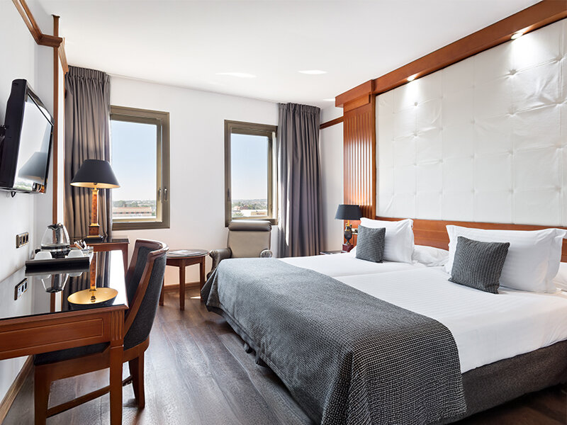 Una habitación de hotel luminosa con cama grande, escritorio y suelo de madera.