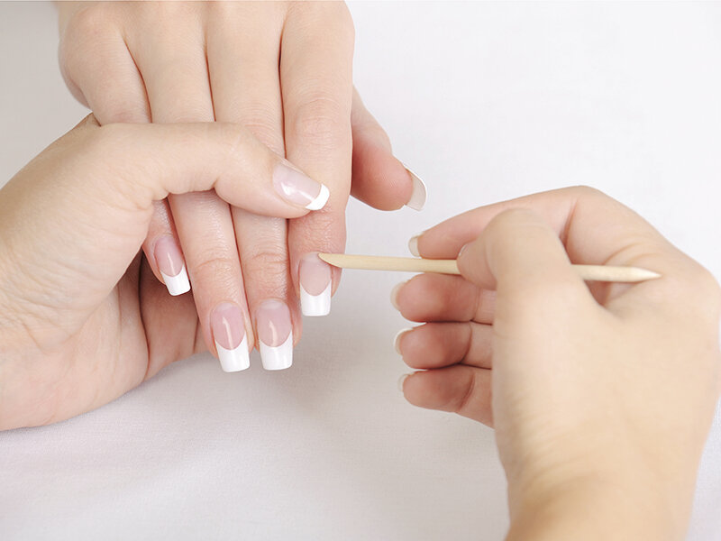 Cuidado de uñas usando un palillo de madera en una mano con manicura francesa.