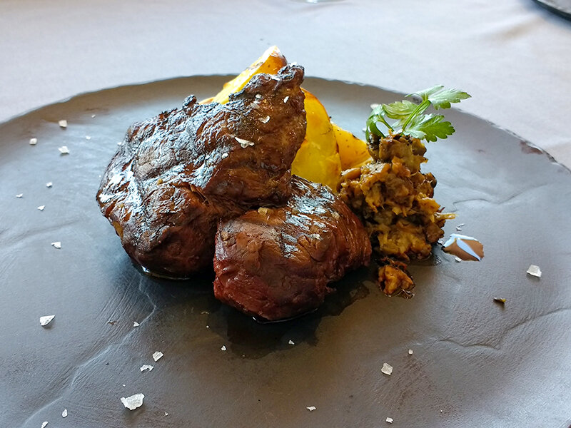 Bistec a la parrilla con patatas y setas en plato negro.