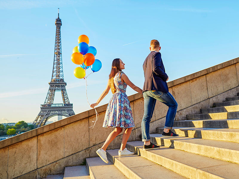 Una pareja sube escaleras de piedra ante la Torre Eiffel, sosteniendo globos.