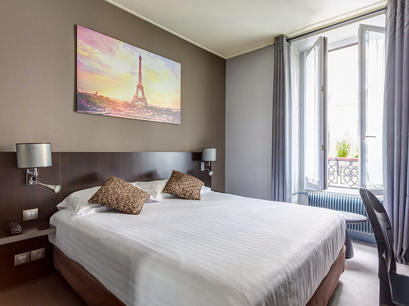 Un dormitorio acogedor con una cama grande, arte de pared de la Torre Eiffel y una ventana abierta.