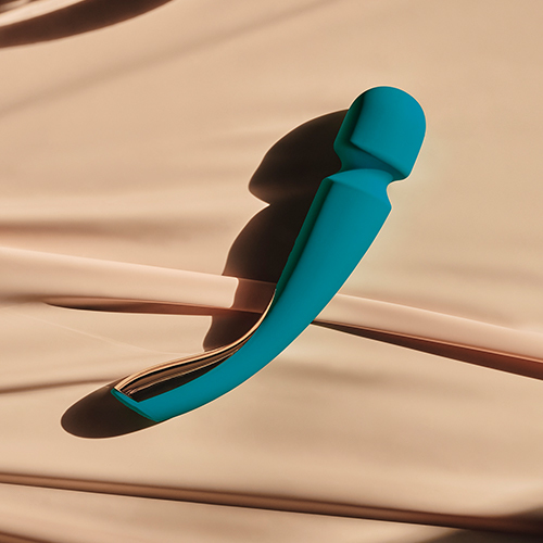 Ein türkisfarbener, gebogener Vibrator liegt auf einer glatten, hautfarbenen Oberfläche mit weichem Schatten.