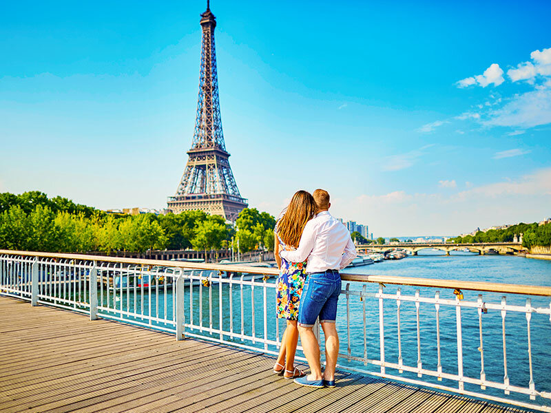 Una pareja está de pie en un puente en París mirando la Torre Eiffel.