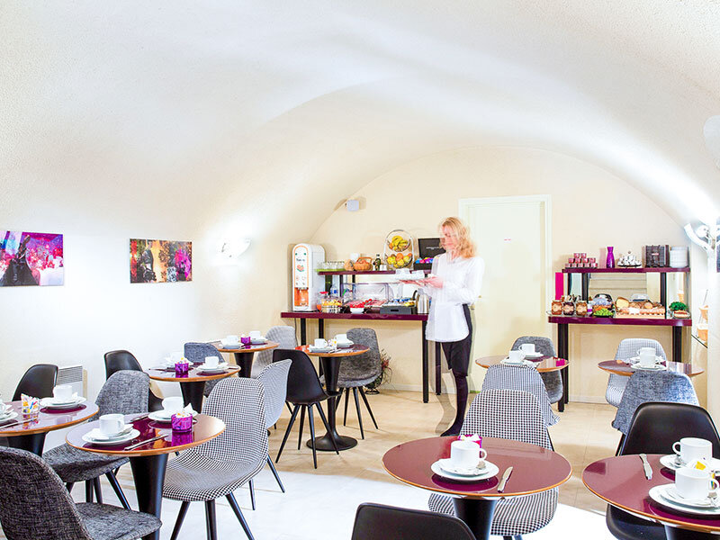Camarera en sala luminosa abovedada con mesas redondas sirve el desayuno.