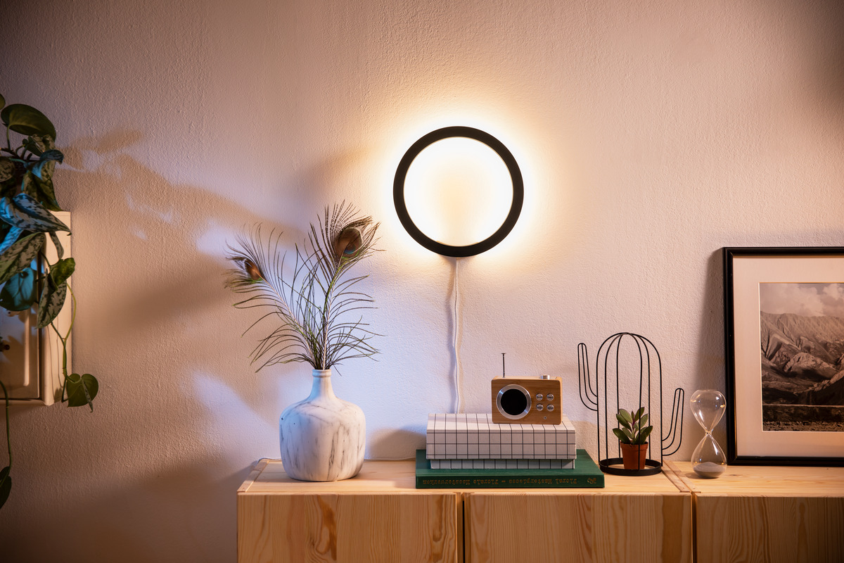 Eine Leuchte an der Wand, eine Vase mit Federn, ein Holztisch, eine Kiste und ein kleines Radio.