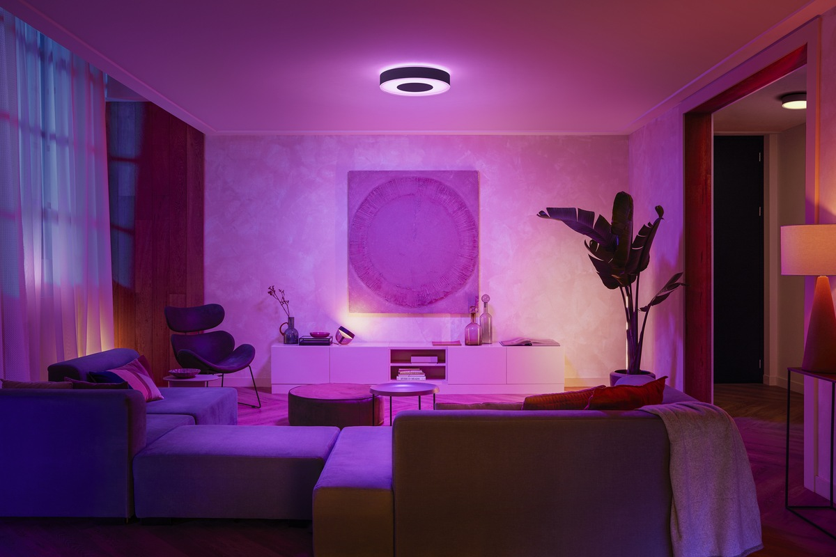 Wohnzimmer mit lilafarbenem Licht, Sofa, runder Deckenleuchte und Kunstwerk.