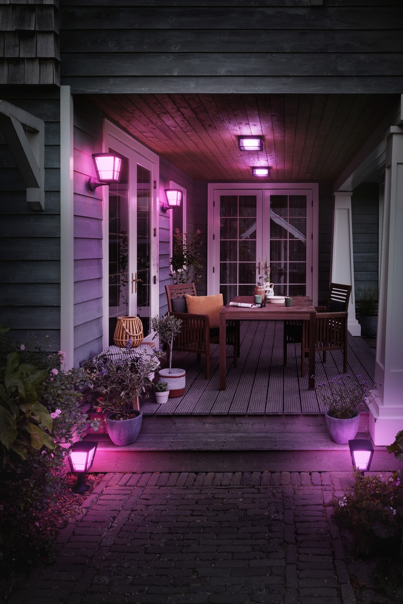 Eine von rosa Außenleuchten beleuchtete Holzterrasse mit Esstisch und Stühlen vor einem Haus.