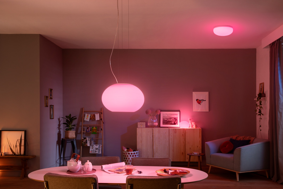 Gemütliches Wohnzimmer mit rosa Beleuchtung, Esstisch, Sesseln und Holzmöbeln.
