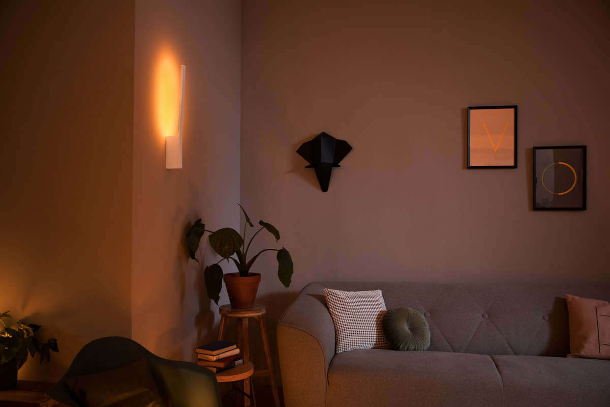 Gemütliches Wohnzimmer mit warmem Wandlicht, grauem Sofa, Kissen, Pflanzen und gerahmter Kunst.