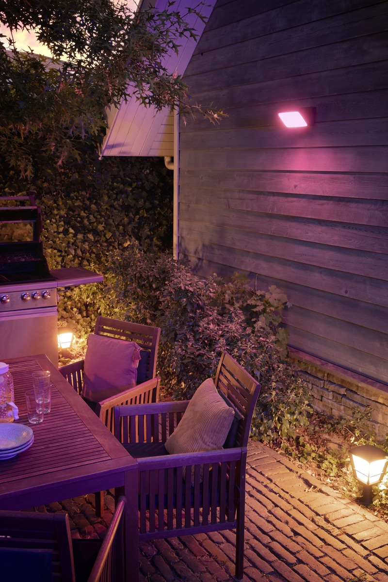 An illuminated wooden patio with a table, chairs, and a wall light at night.