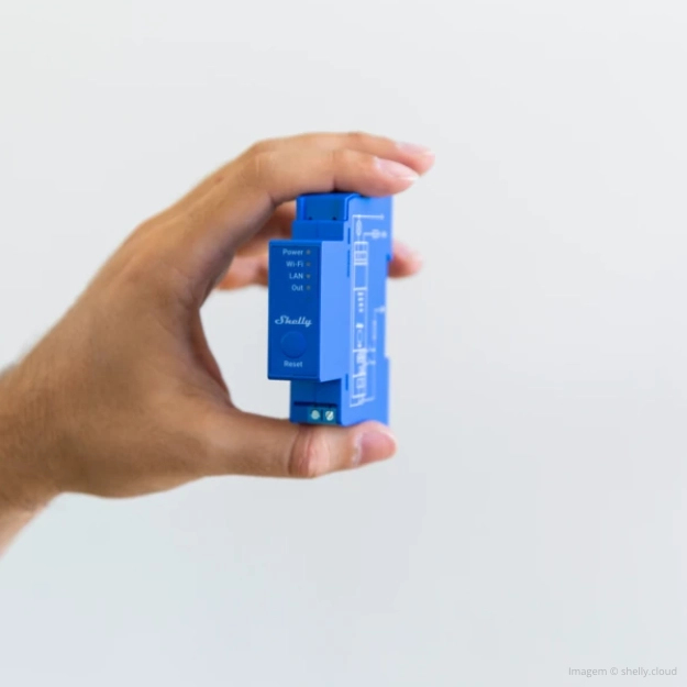 Una mano tiene in mano un dispositivo elettronico Shelly blu su sfondo chiaro.